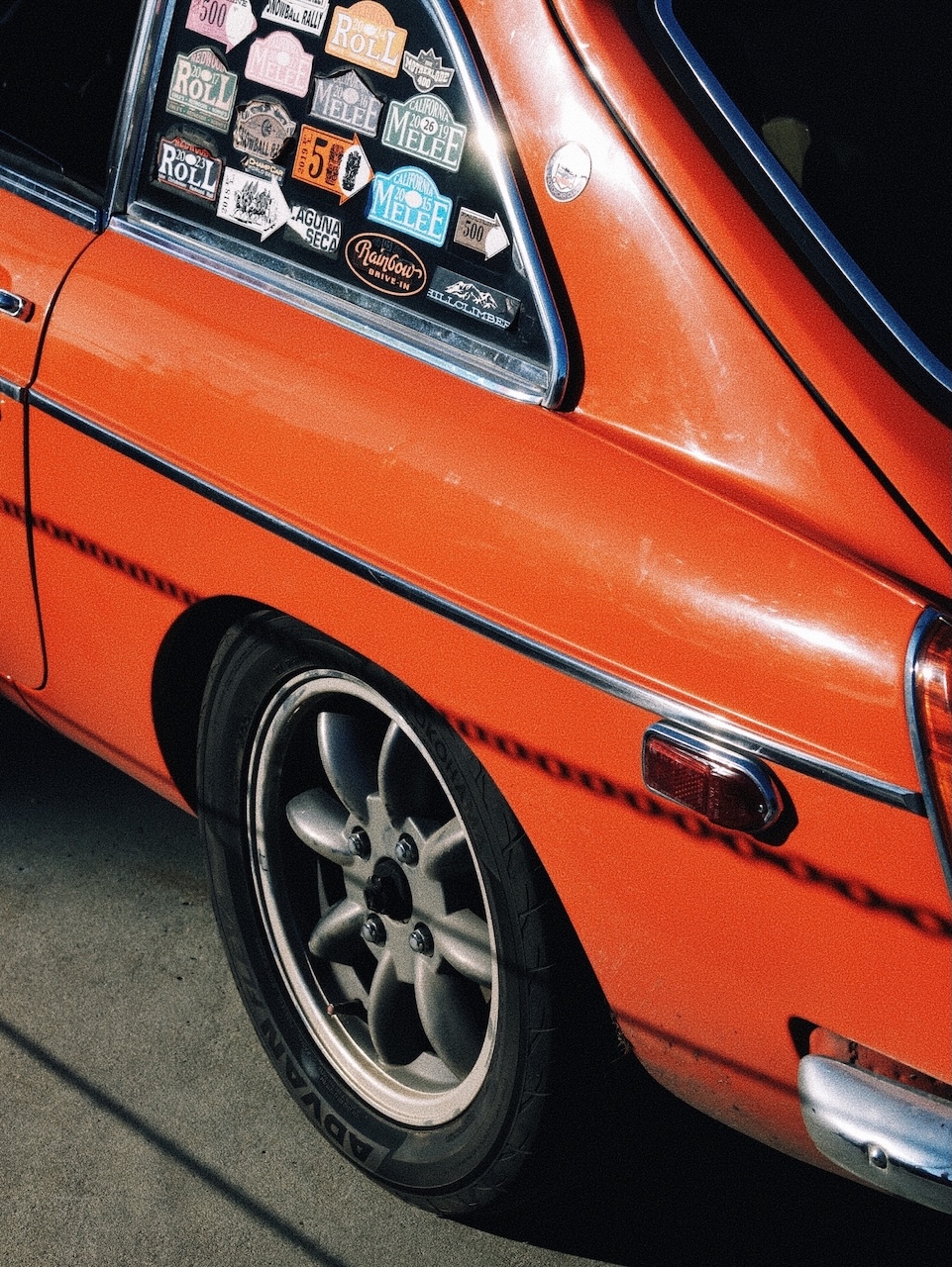 Red vintage car. A wheel and part of the rear is shown. Lots of stickers on the window.